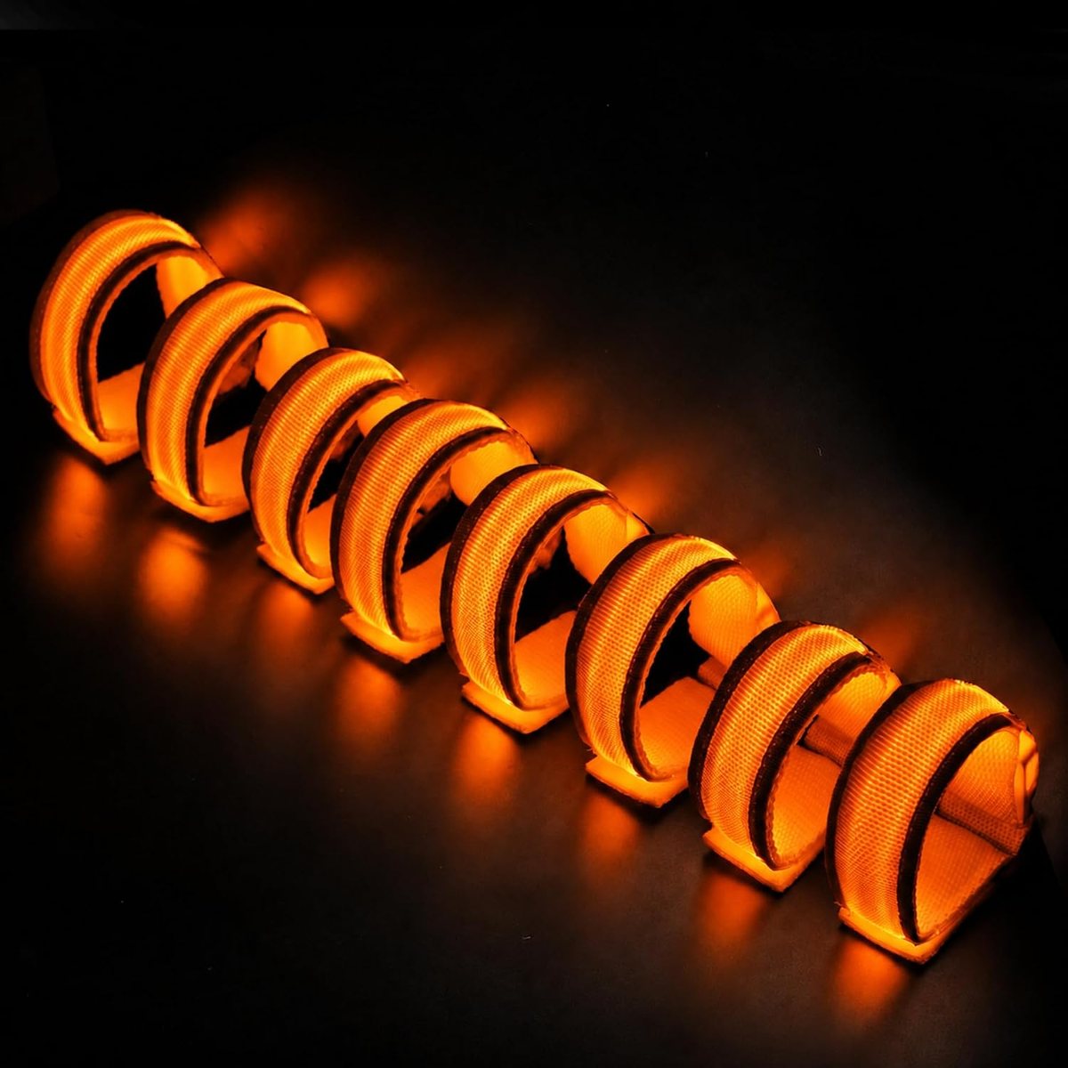 Eight FANL orange LED glow bracelets glowing against a dark autumn background