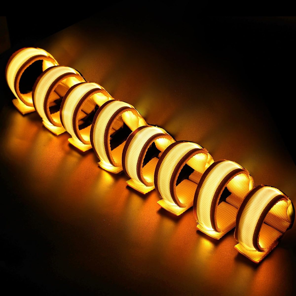 Eight FANL yellow LED glow bracelets lit on a dark background